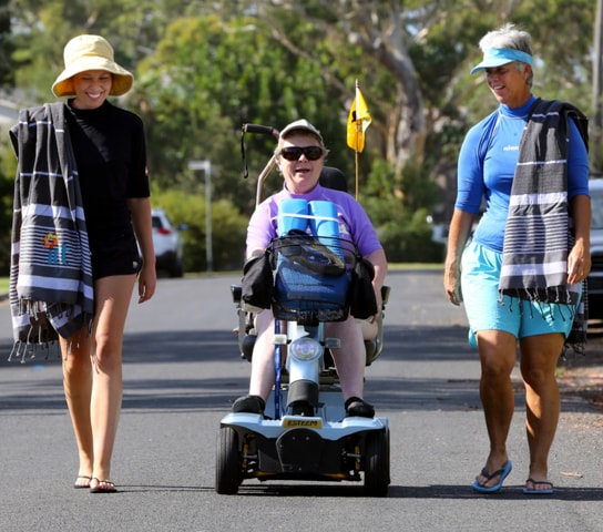 Two women walking with an eldery women in a mobility scooter