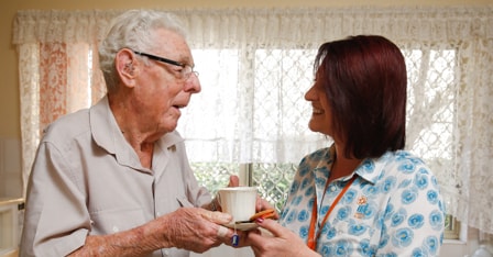 An elderly man holding a cup of tea with an IRT carer in his assisted living community