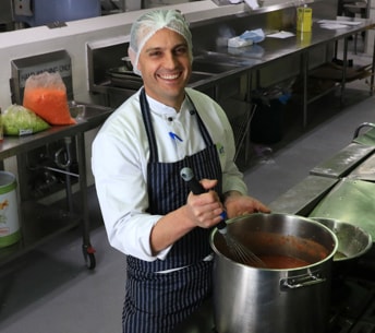 IRT Catering male employee stirring a pot in a commercial kitchen