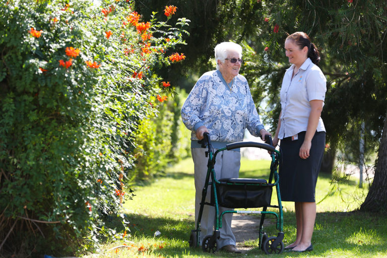 An elderly woman with a walking frame outside with an IRT carer