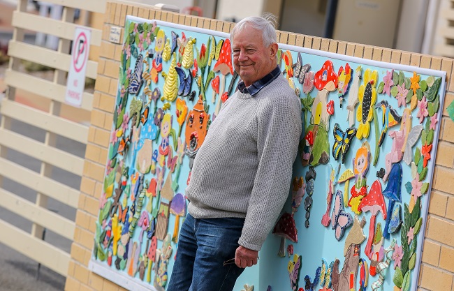 Our residents embrace creativity and an example is IRT Macarthur pottery teacher Michael Bright. He is standing in front of the community’s pottery wall.